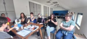 Egy tagunknak a jeltolmács tolmácsolja az előadó szavait, háttérben több résztvevő is látszik