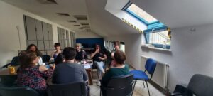 Asztal körül a résztvevők, egy tagunk éppen egy kérdést tesz fel az előadónak